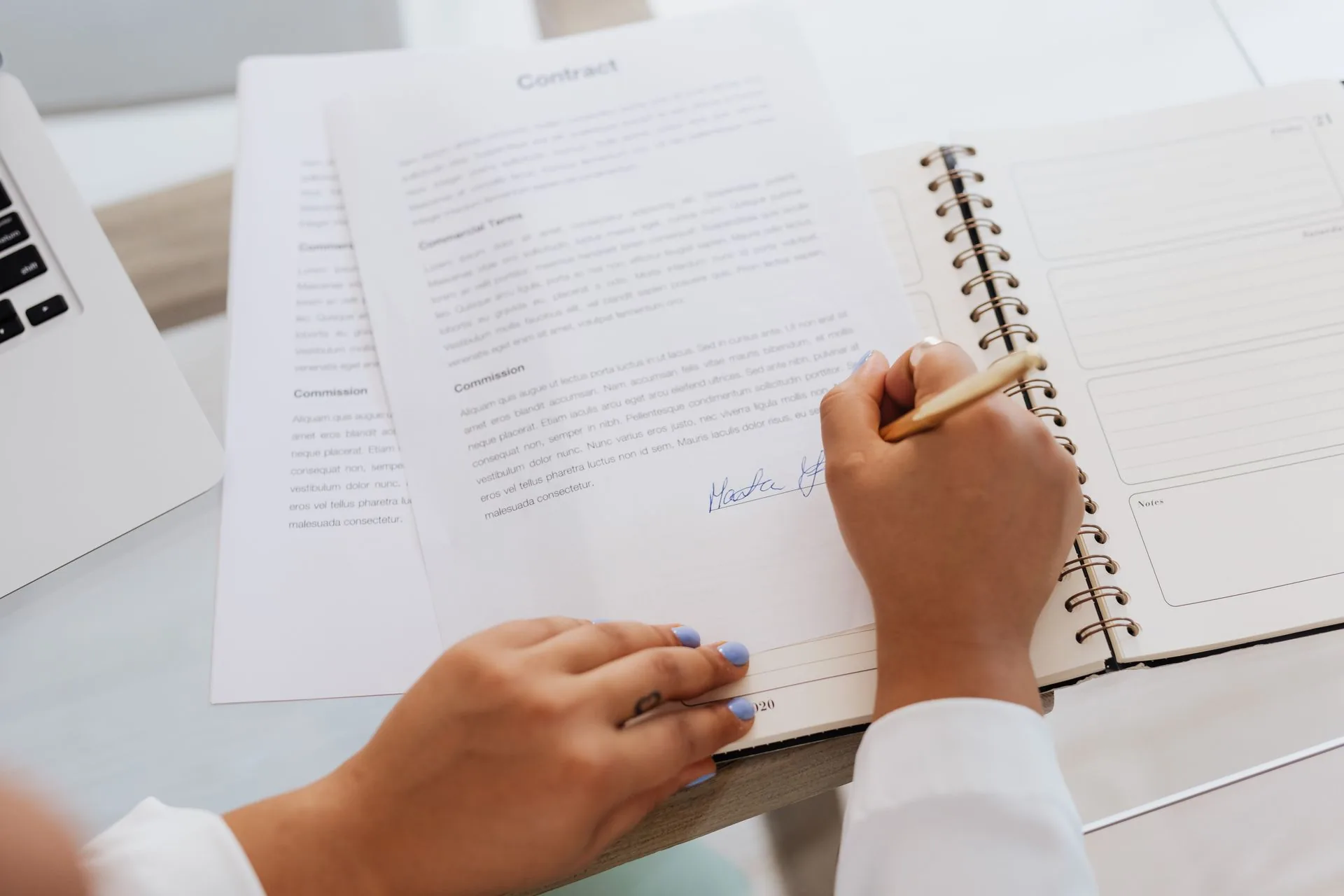 Mãos com caneta sobre documentos e uma agenda em uma mesa.