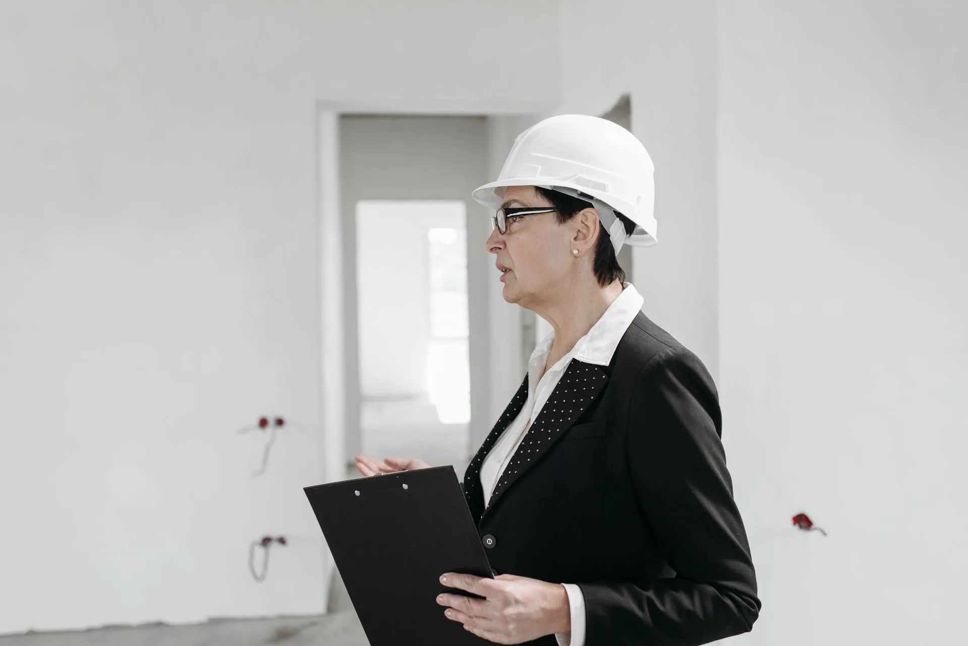 Profissional com capacete branco e prancheta em um ambiente em construção.