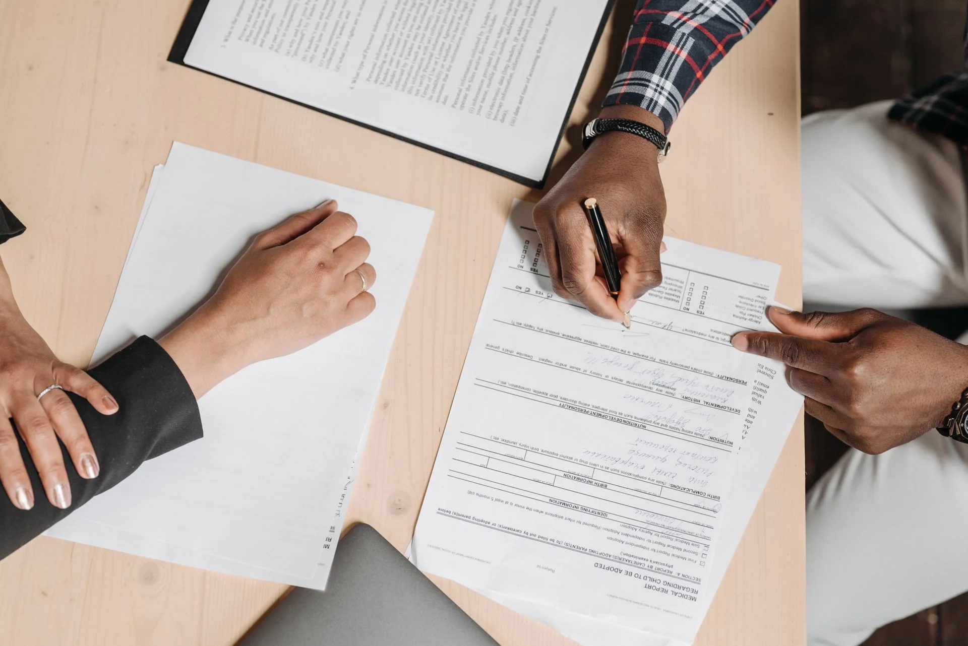 Pessoas examinam documentos e fazem anotações sobre uma mesa de trabalho.